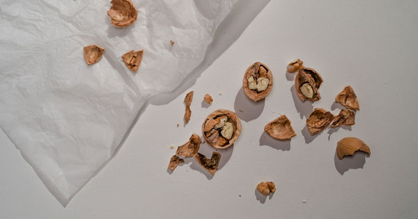 Cracked walnut shells scattered on a white surface beside crumpled paper.
