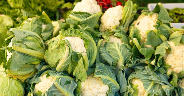 Pile of fresh cauliflowers with green leaves at an open-air market. Perfect for healthy lifestyle themes.