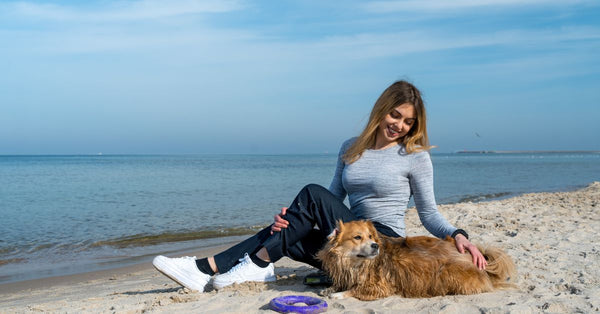 Woman enjoying a sunny day at Kołobrzeg beach with her dog, capturing a perfect seaside moment.