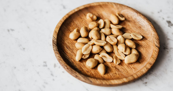 Top view of roasted peanuts in a wooden plate placed on a marble surface.