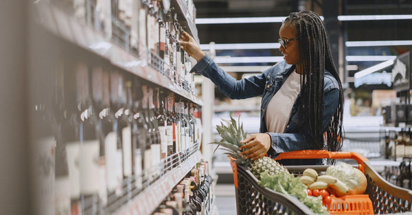 A woman shopping for wine and groceries, filling her cart with fresh produce.