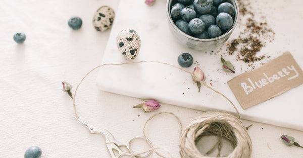 A flat lay featuring blueberries, quail eggs, and craft materials in a soft, natural light.