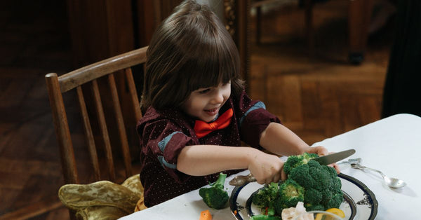 Young child excitedly cutting broccoli during a healthy meal at home.