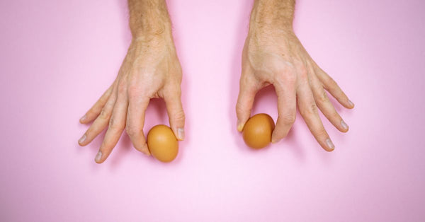 Close-up of hands holding two brown eggs on a pastel pink background, minimalist, creative.