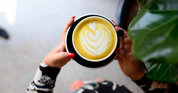 An aerial shot of colorful latte art in a black cup held by hands.