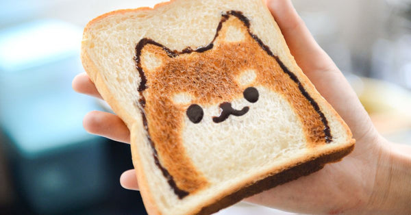 Adorable Shiba Inu face toast art, perfect for breakfast fun, held by hand in a bright setting.