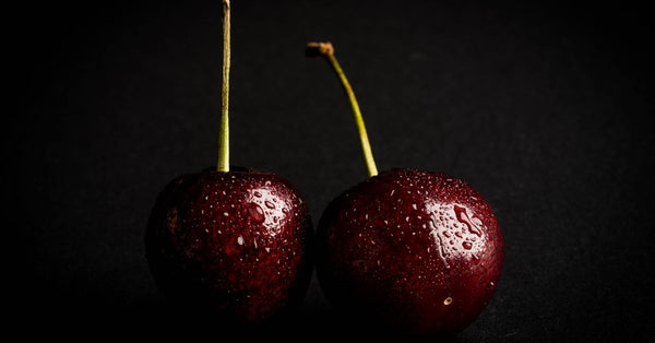 Detailed image of fresh cherries with water droplets on a black background, highlighting their vibrant red color.