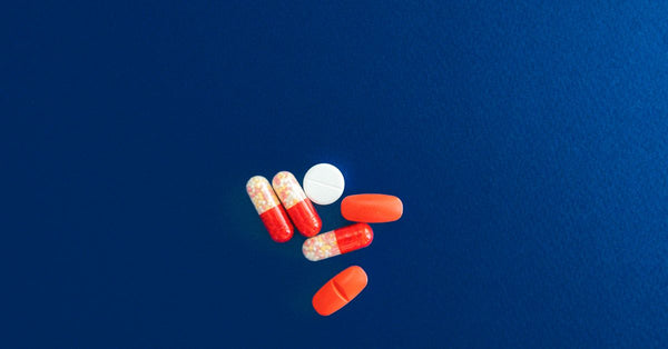 Assorted red and white capsules and tablets on a vivid blue surface.